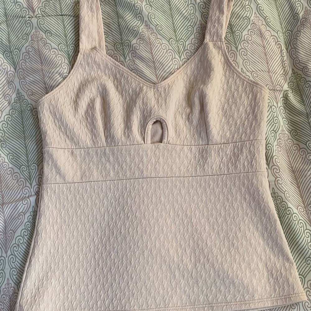 A cream color crop top with a opening/ hole in the center of the chest.
